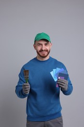 Photo of Man with paintbrush and color samples on light grey background