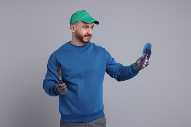 Photo of Man with paintbrush and color samples on light grey background