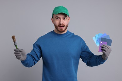 Photo of Emotional man with paintbrush and color samples on light grey background