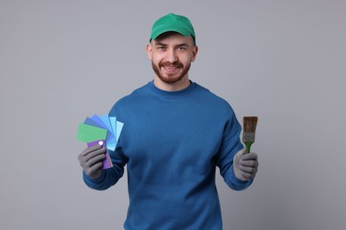 Photo of Man with paintbrush and color samples on light grey background