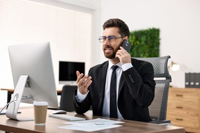 Photo of Man talking on smartphone while working at table in office