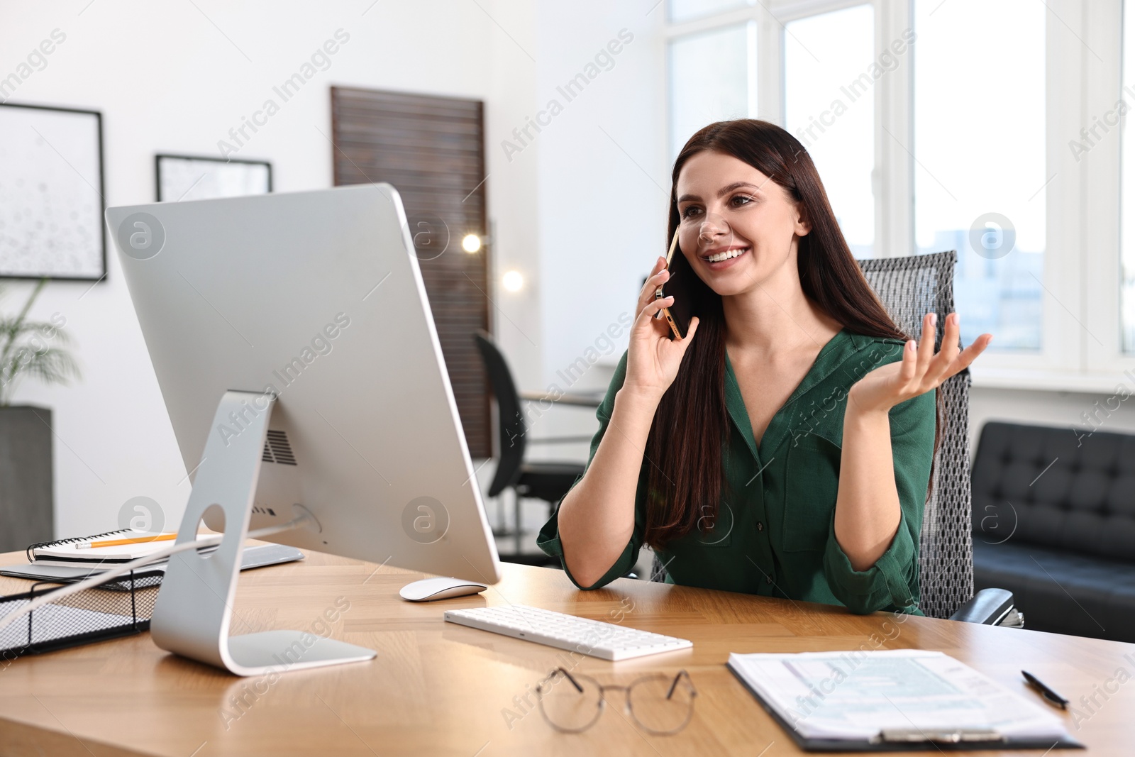 Photo of Woman talking on smartphone while working at table in office