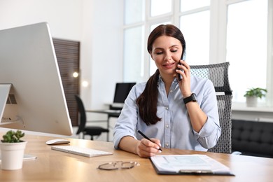 Photo of Woman talking on smartphone while working at table in office