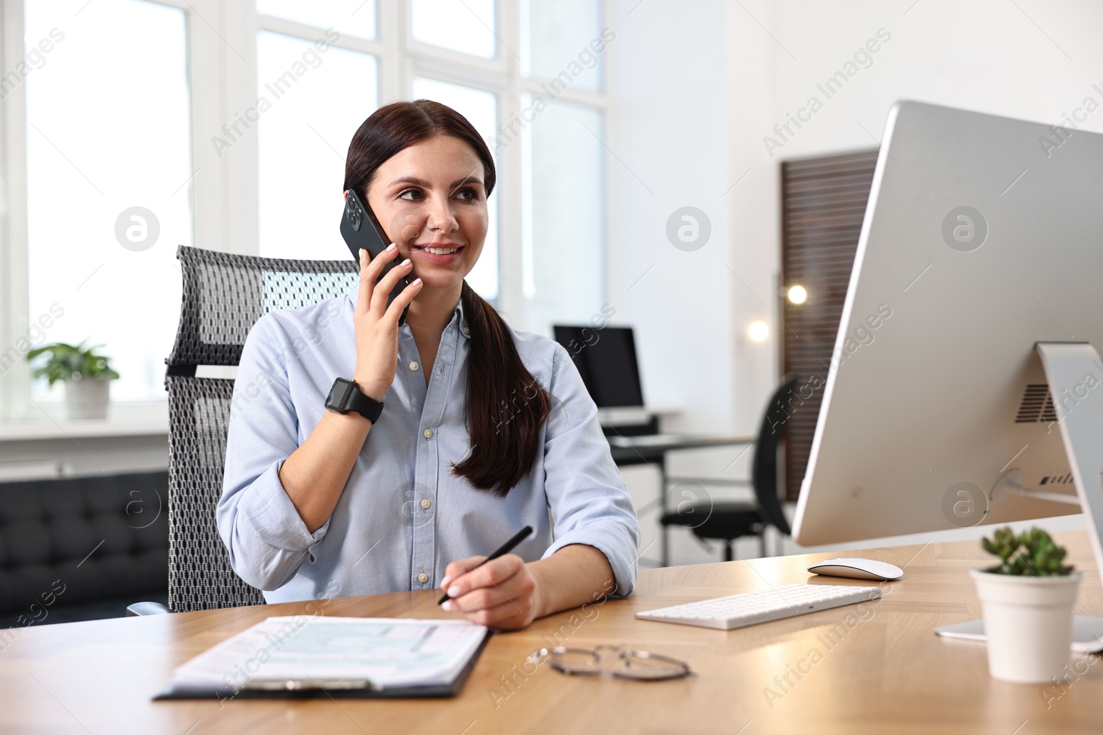 Photo of Woman talking on smartphone while working at table in office