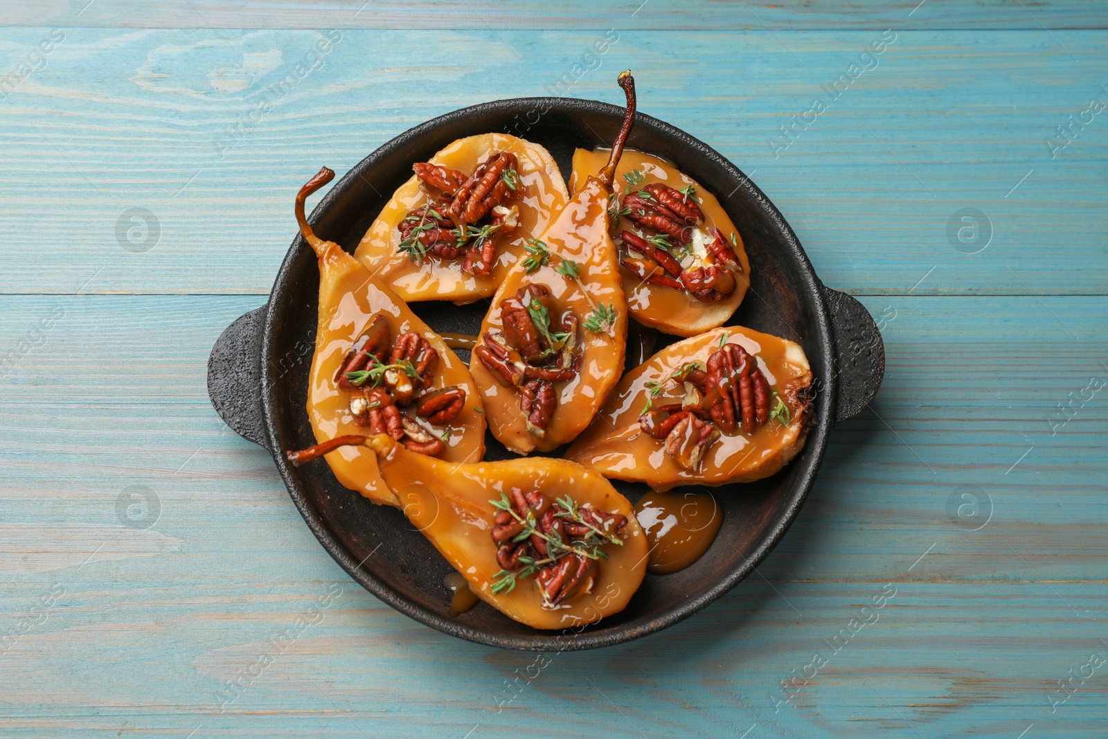 Photo of Delicious pears with caramel sauce, pecan nuts and thyme on light blue wooden table, top view