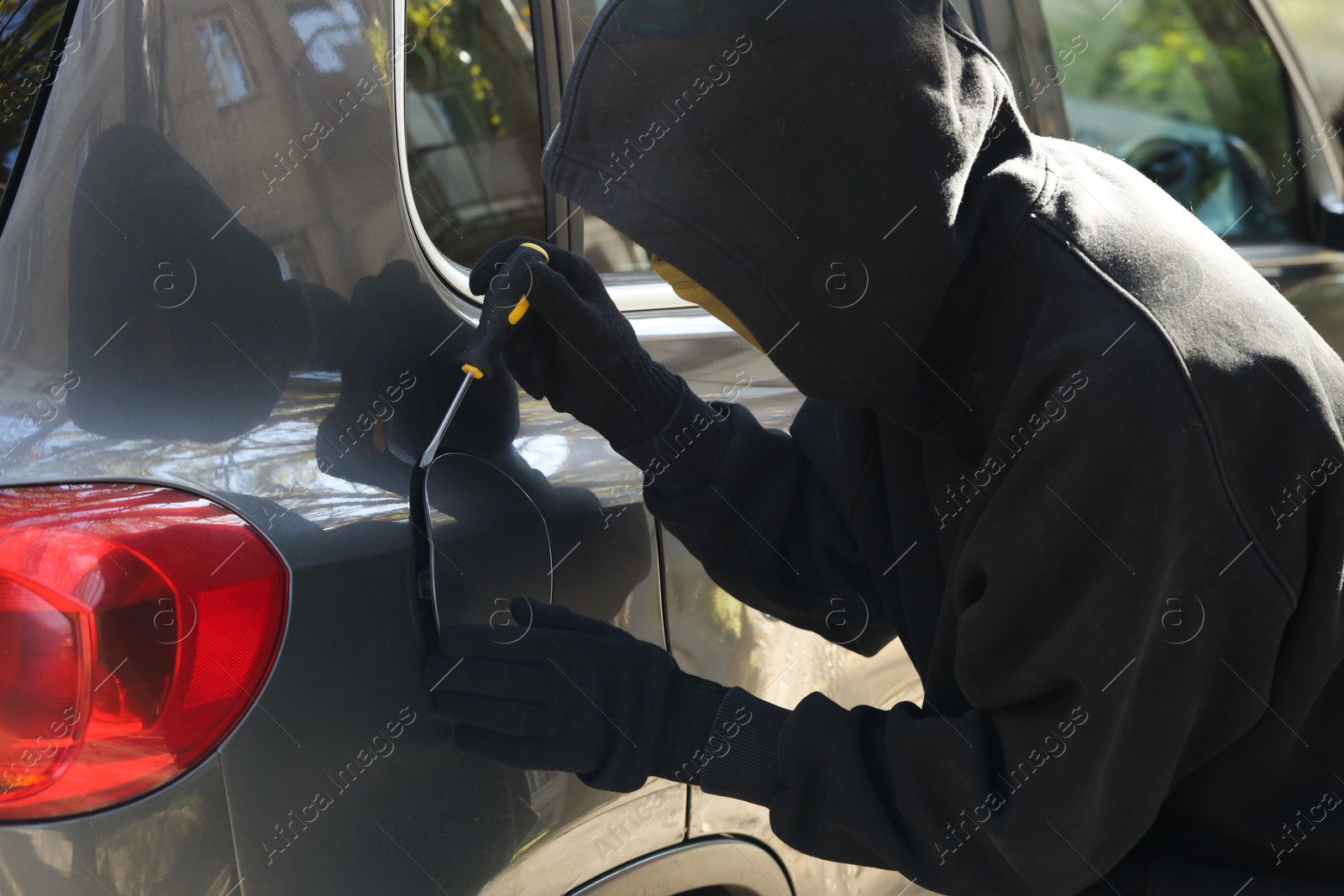 Photo of Thief with screwdriver opening fuel cap. Car hijacking