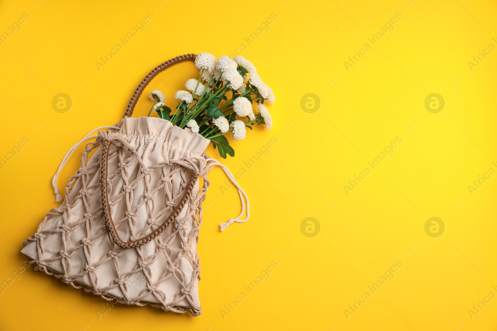 Photo of Macrame shopping bag with flowers on yellow background, top view. Space for text