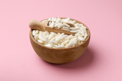 Photo of Puffed rice in bowl and scoop on light pink background, closeup