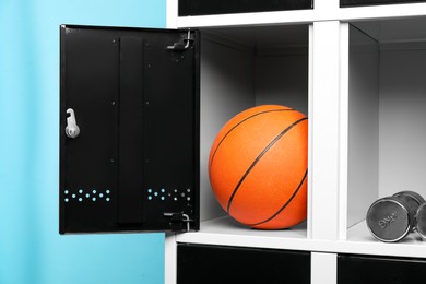 Photo of Open lockers with basketball ball and dumbbells on light blue background