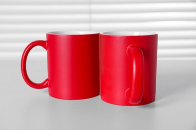 Photo of Blank red ceramic mugs on white table. Mockup for design