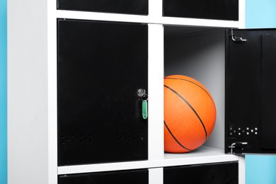 Photo of Open locker with basketball ball on light blue background, closeup