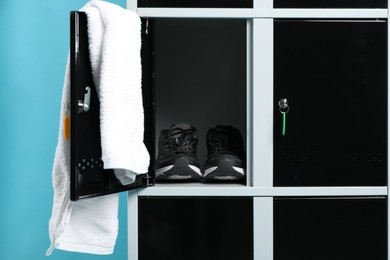 Photo of Open locker with sneakers and towel on light blue background