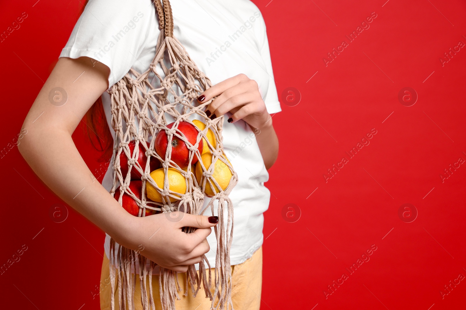 Photo of Teenage girl with handmade macrame bag on red background, closeup. Space for text