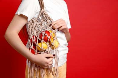 Photo of Teenage girl with handmade macrame bag on red background, closeup. Space for text