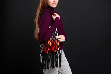 Photo of Teenage girl with handmade macrame bag on black background, closeup