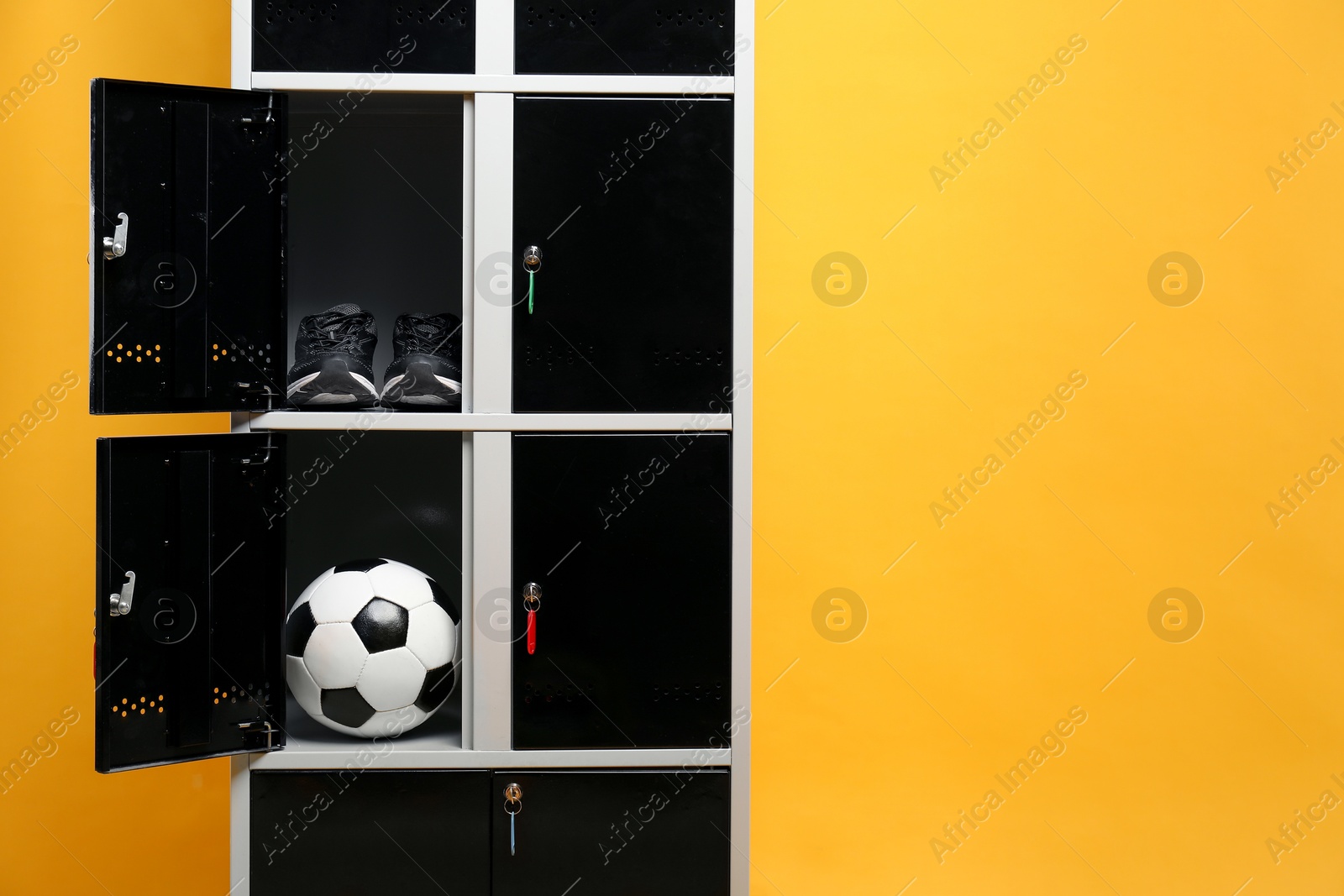 Photo of Open lockers with sneakers and soccer ball on orange background, space for text