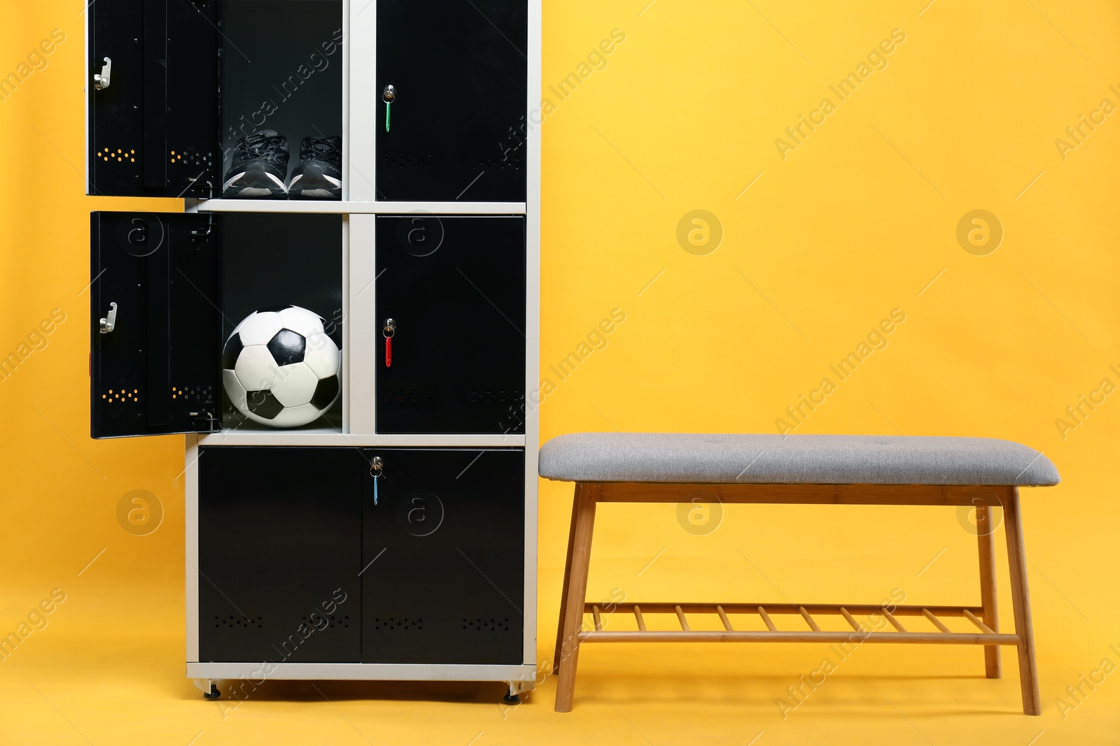 Photo of Open lockers with soccer ball, sneakers and bench on orange background