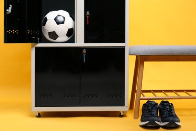 Photo of Open locker with soccer ball, bench and sneakers on orange background