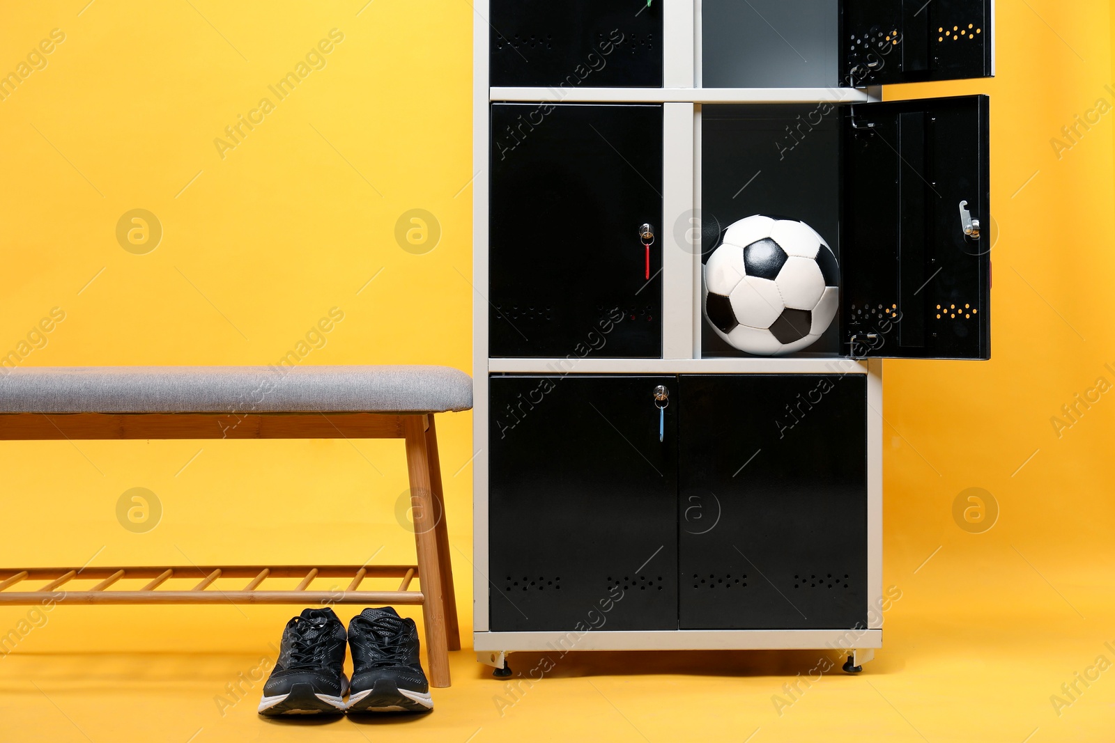 Photo of Open locker with soccer ball, bench and sneakers on orange background