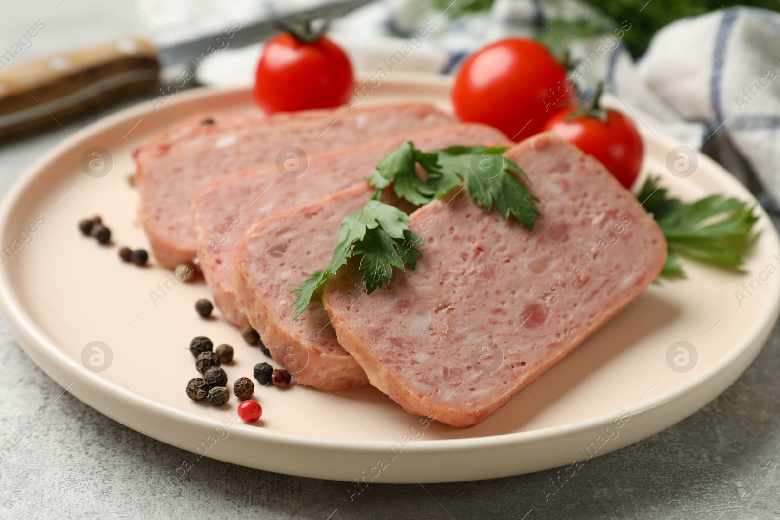 Photo of Pieces of tasty canned meat, parsley, peppercorns and tomatoes on grey textured table, closeup