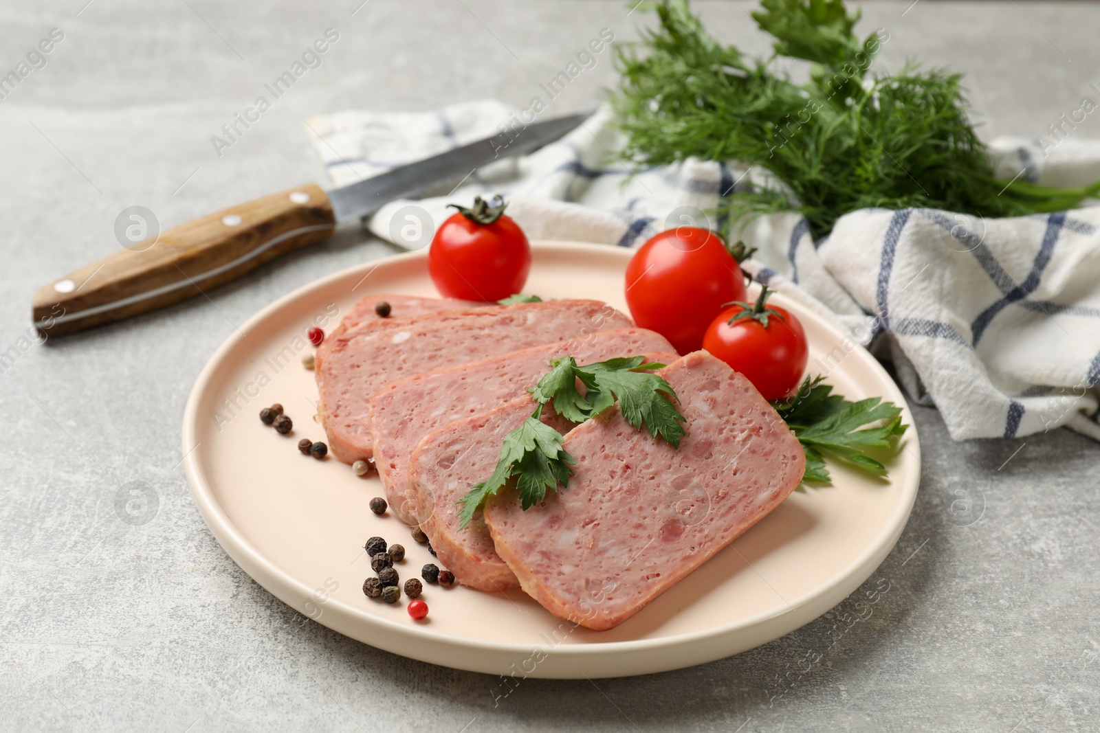 Photo of Pieces of tasty canned meat, parsley, peppercorns and tomatoes on grey textured table, closeup