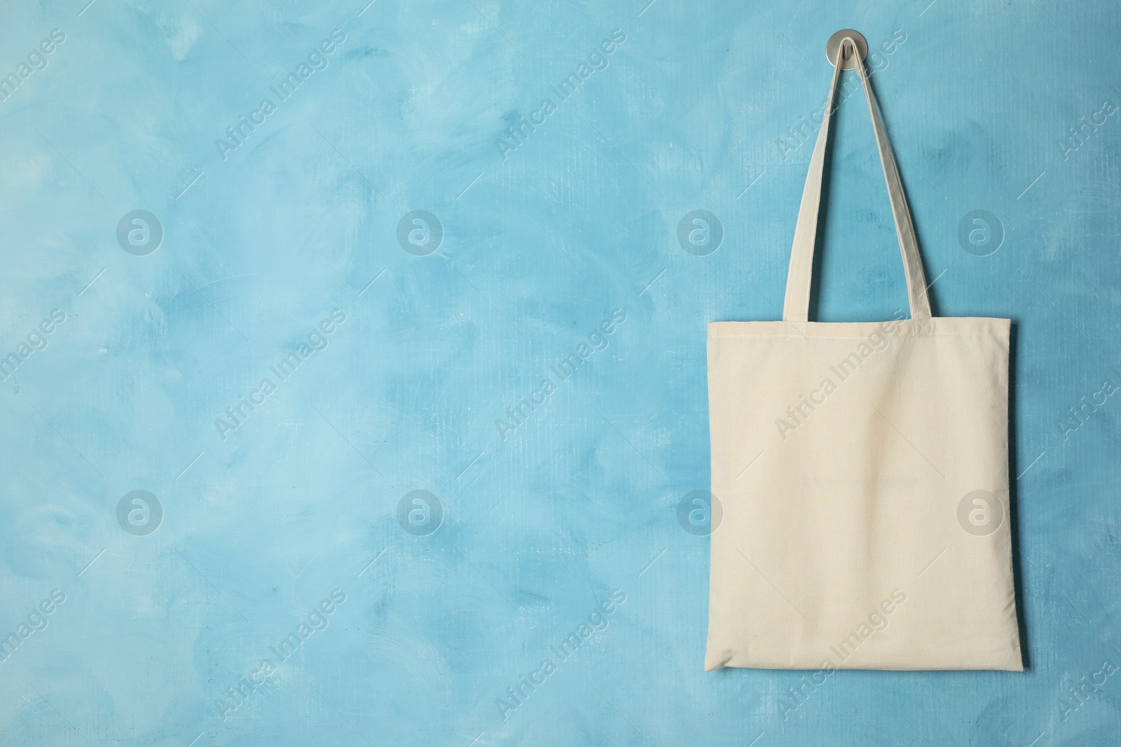 Photo of Eco bag hanging on light blue wall. Mockup for design