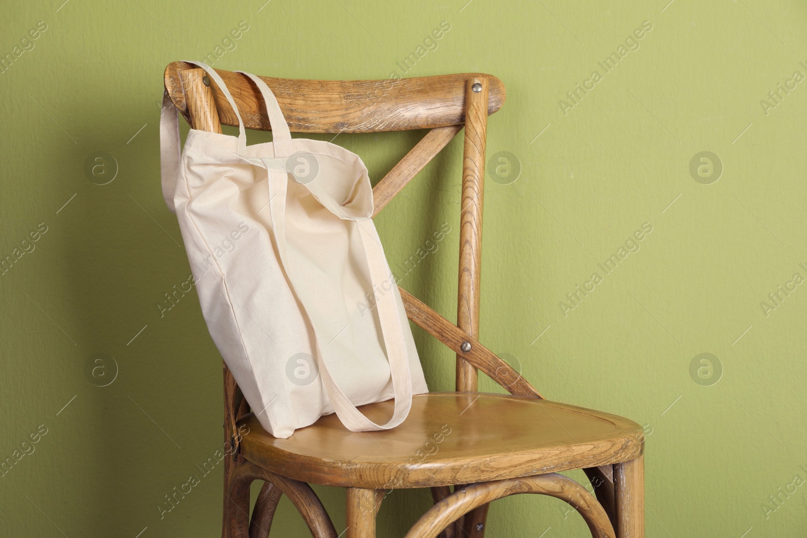 Photo of One eco bag on wooden chair near green wall. Mockup for design