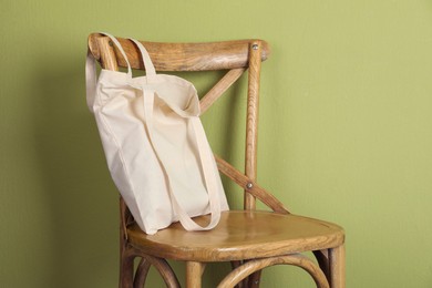 Photo of One eco bag on wooden chair near green wall. Mockup for design