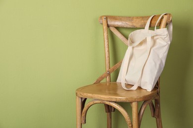 Photo of One eco bag on wooden chair near green wall. Mockup for design