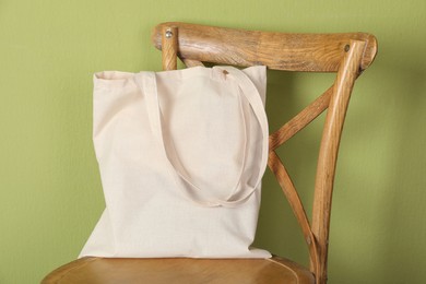 Photo of One eco bag on wooden chair near green wall. Mockup for design