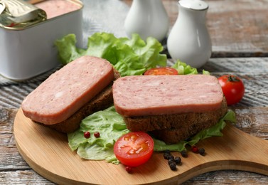 Tasty canned meat, bread, tomatoes, spices and lettuce on wooden table, closeup