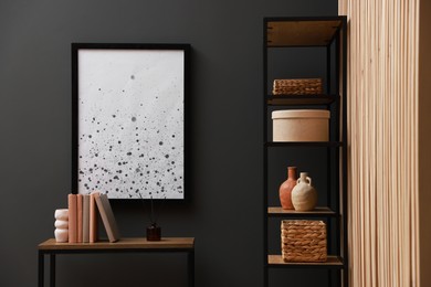 Photo of Console table with decor and shelving unit near grey wall in room. Interior design