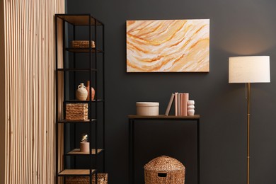 Photo of Console table with decor, shelving unit and lamp near grey wall in room. Interior design