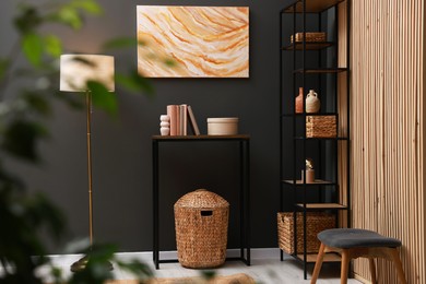 Photo of Console table with decor, shelving unit and lamp near grey wall in room. Interior design