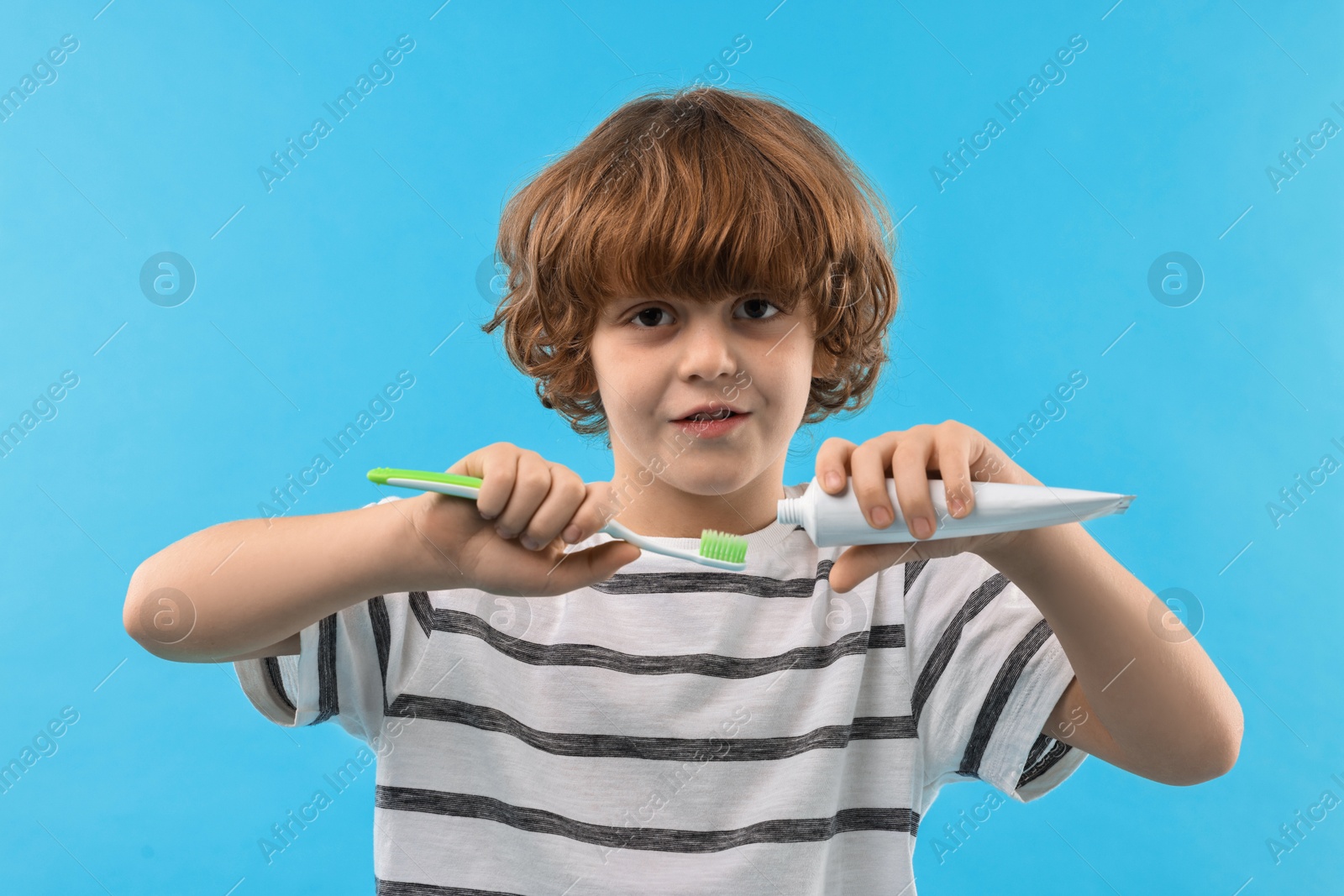 Photo of Cute boy applying paste on toothbrush against light blue background