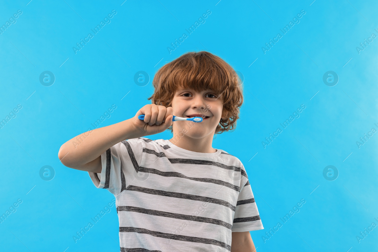 Photo of Cute boy brushing his teeth on light blue background