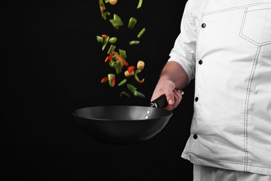 Photo of Professional chef mixing vegetables in wok on black background, closeup