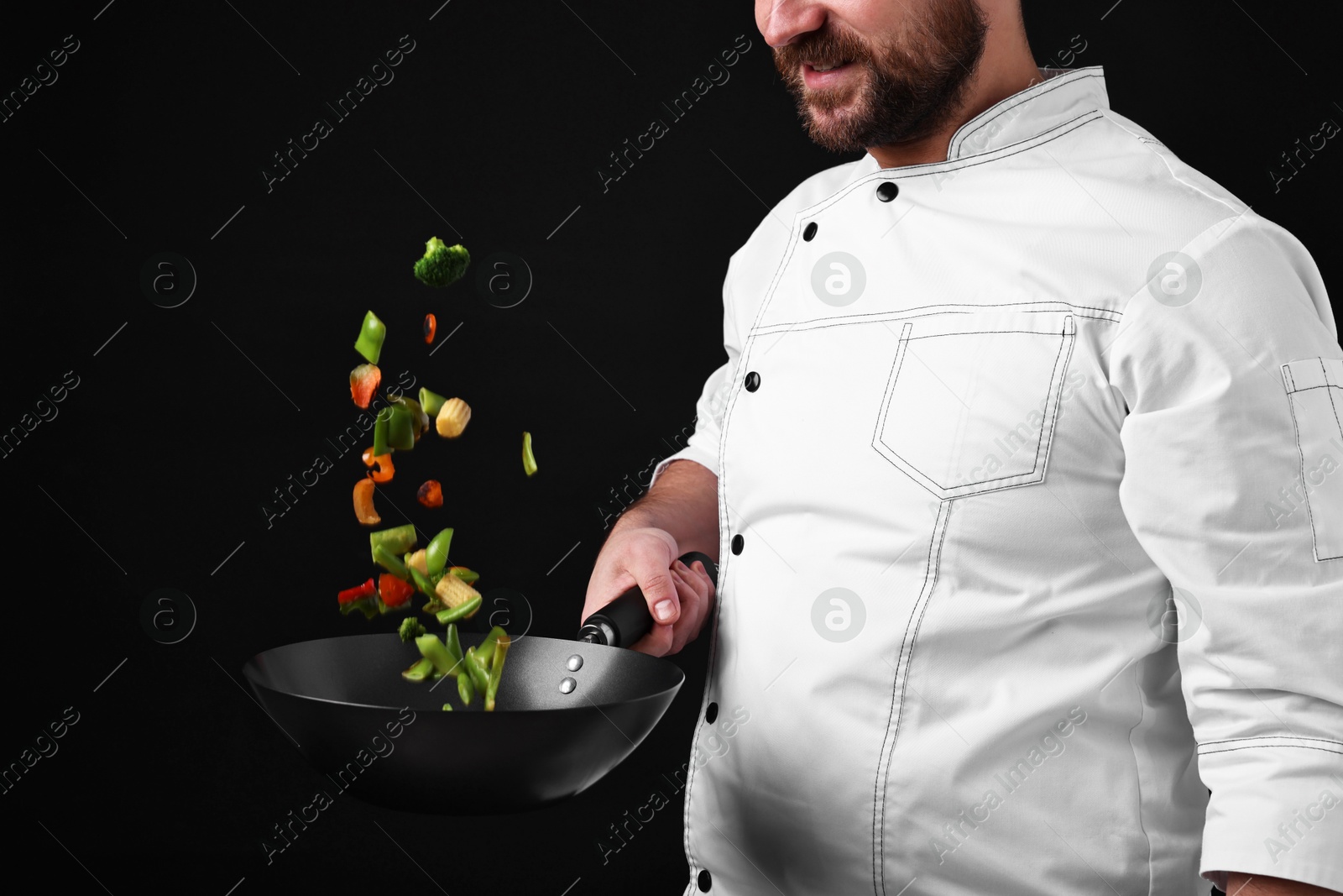 Photo of Professional chef mixing vegetables in wok on black background, closeup