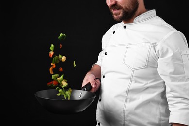 Photo of Professional chef mixing vegetables in wok on black background, closeup