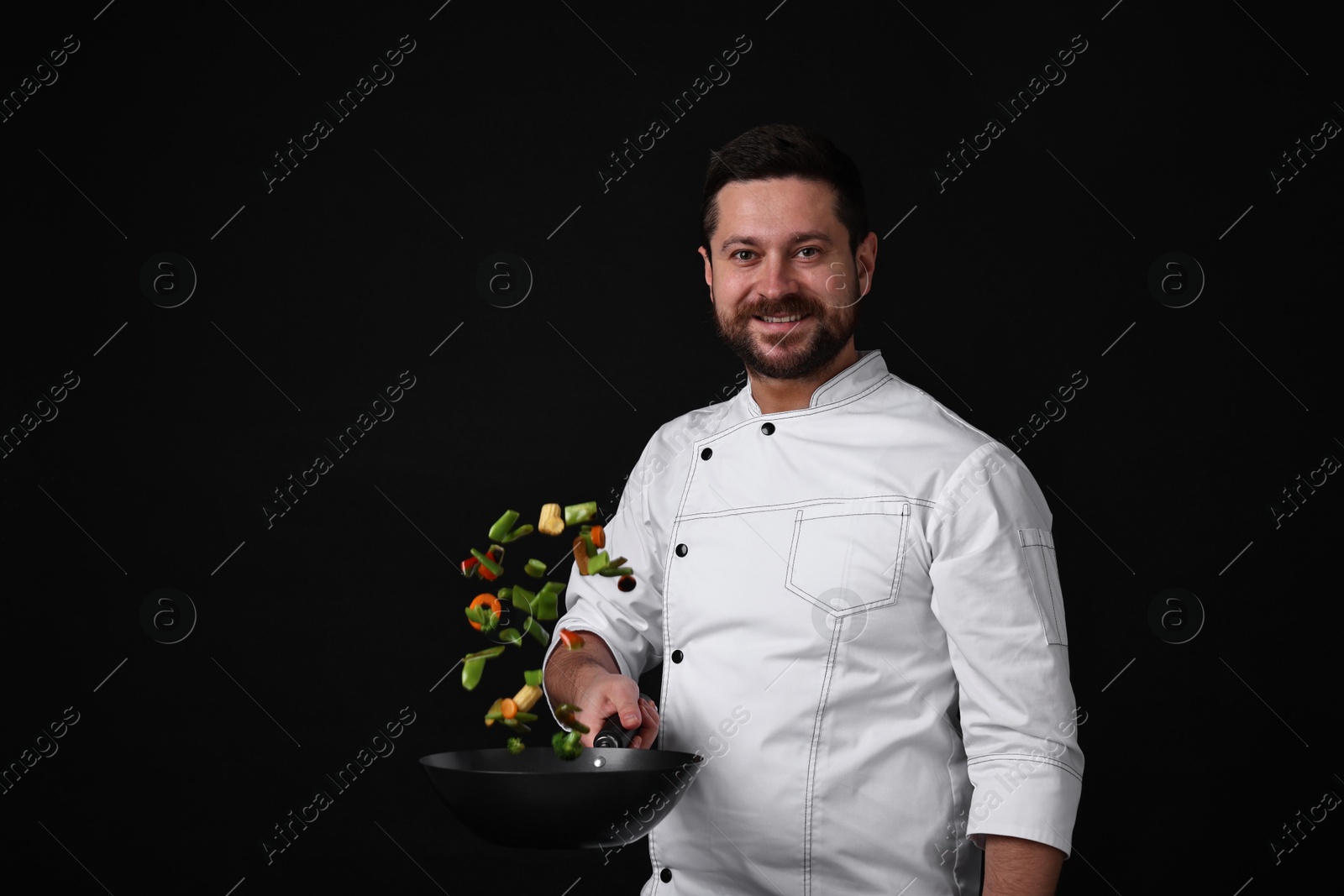 Photo of Professional chef mixing vegetables in wok on black background. Space for text