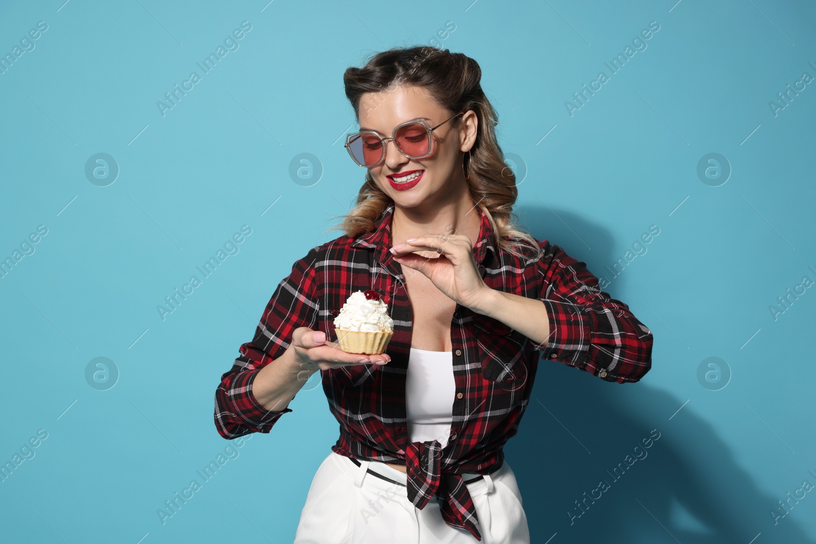 Photo of Happy pin-up woman with cupcake on light blue background