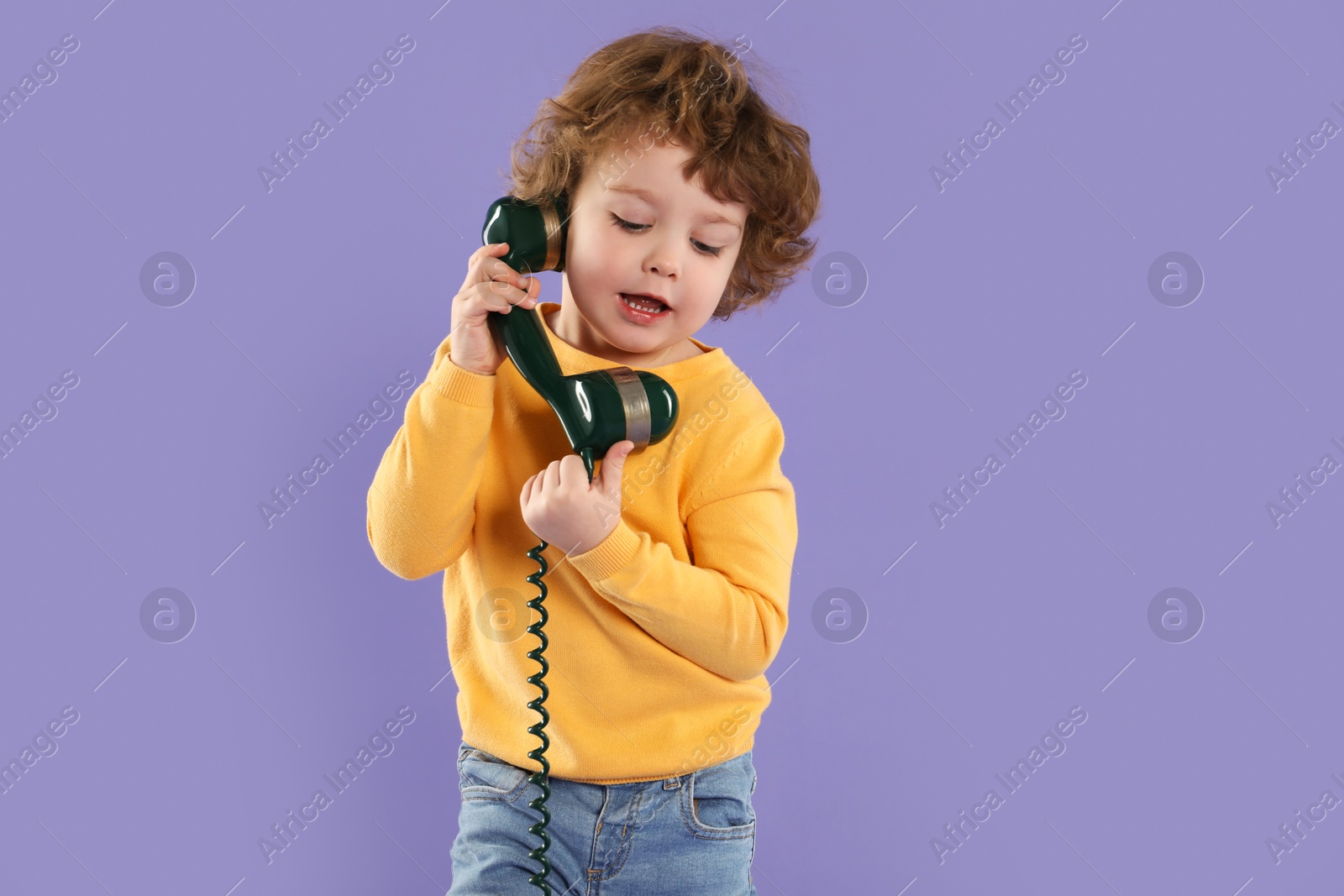 Photo of Cute little boy with telephone handset on violet background