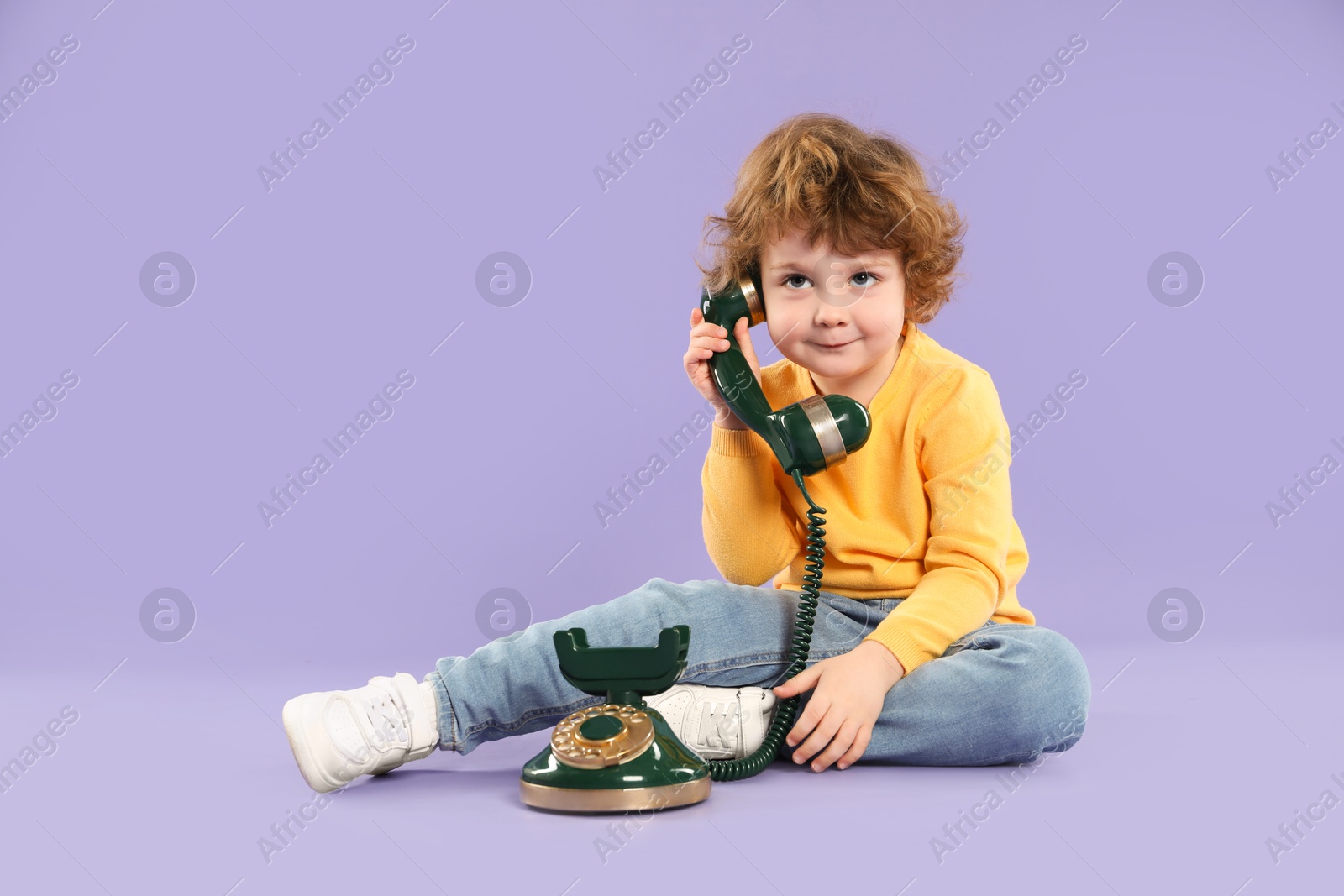 Photo of Cute little boy with old telephone on violet background