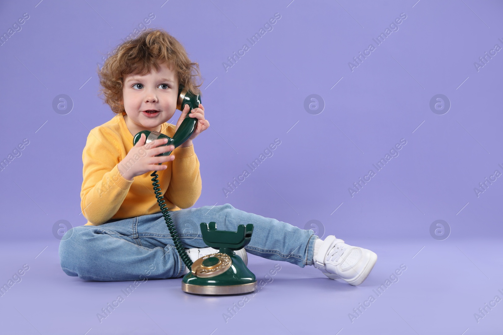 Photo of Cute little boy with old telephone on violet background, space for text