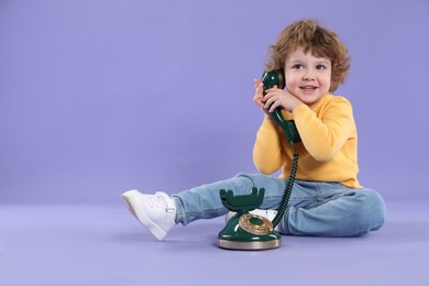 Photo of Cute little boy with old telephone on violet background, space for text