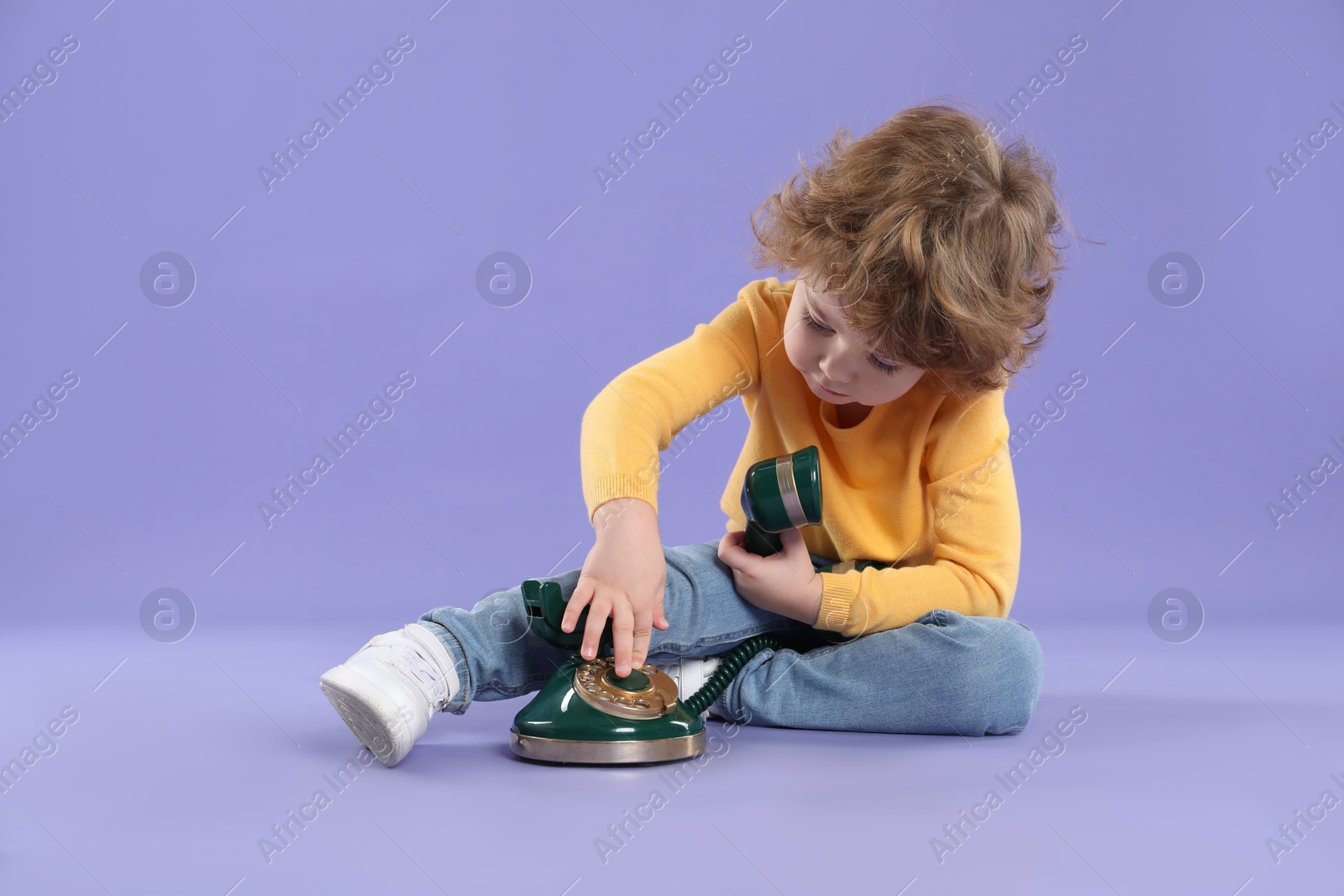 Photo of Cute little boy with old telephone on violet background