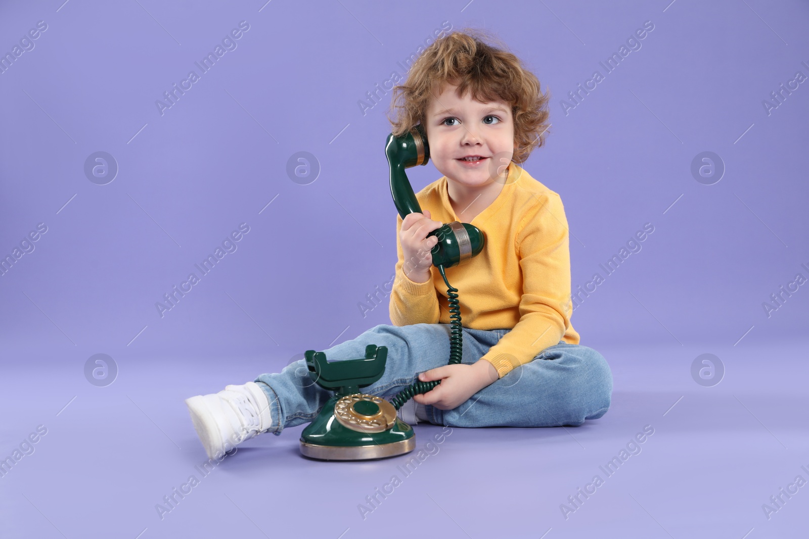 Photo of Cute little boy with old telephone on violet background