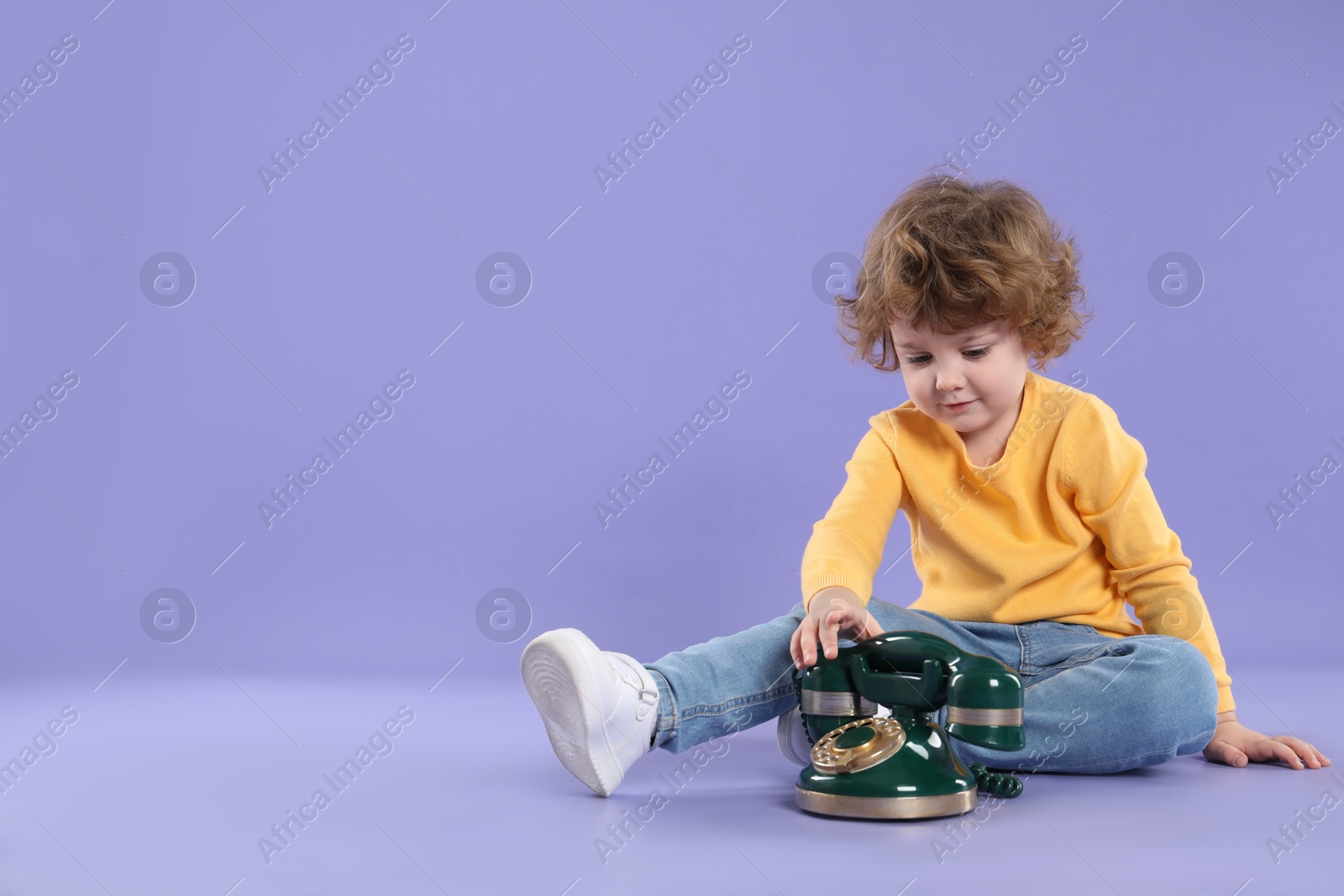 Photo of Cute little boy with old telephone on violet background, space for text