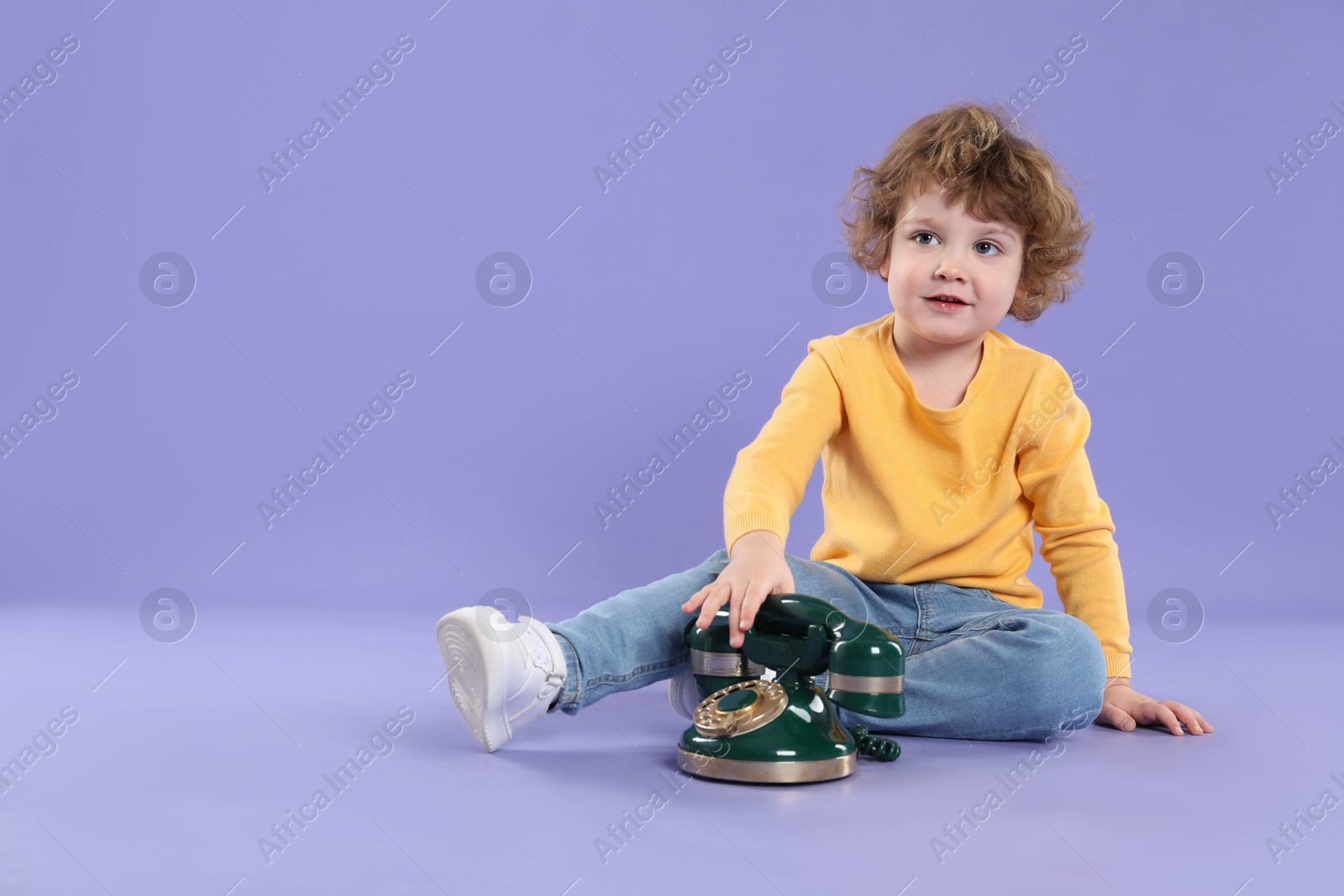 Photo of Cute little boy with old telephone on violet background, space for text