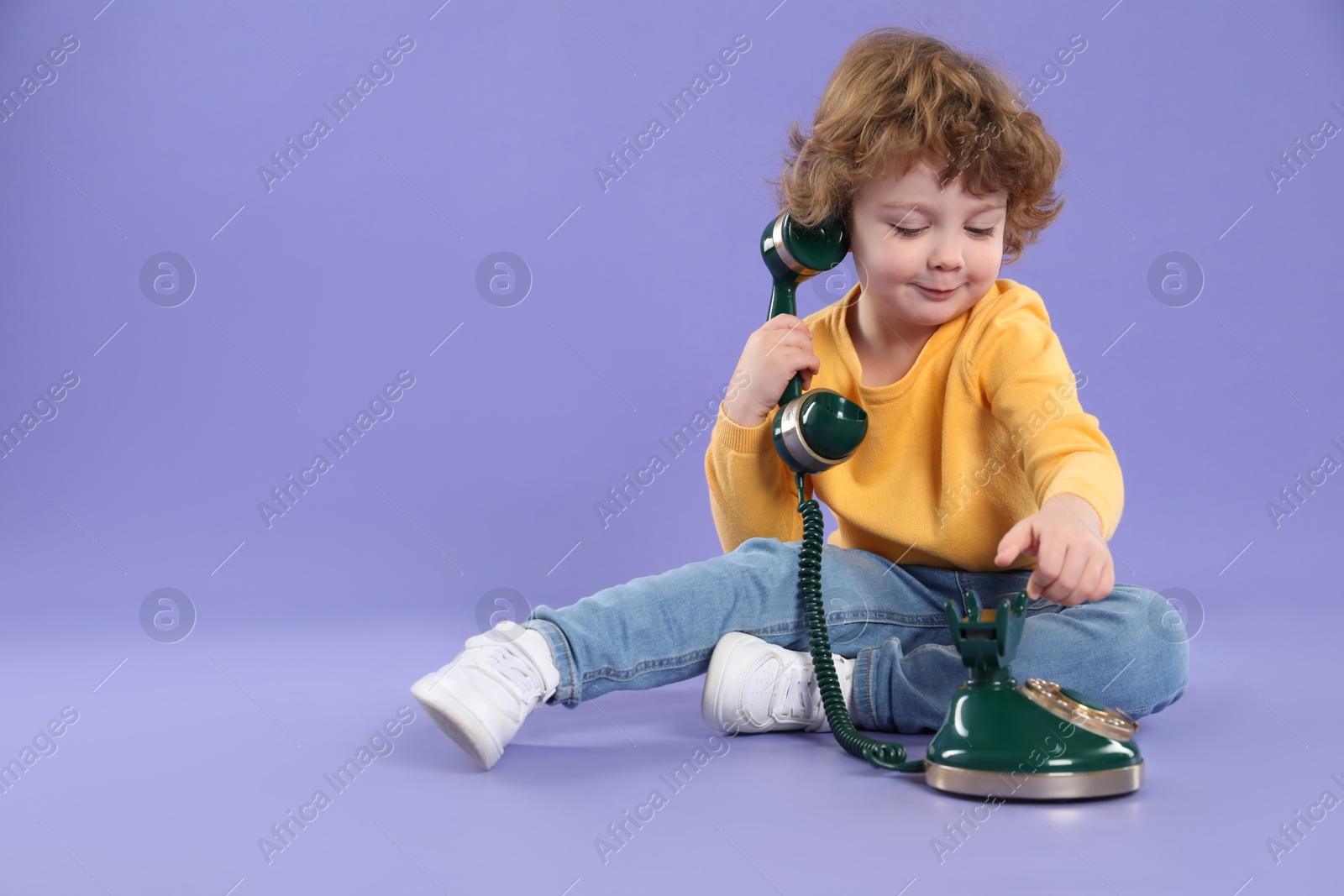 Photo of Cute little boy with old telephone on violet background, space for text